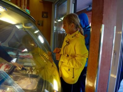 a girl in a yellow jacket standing next to a glass case of ice cream