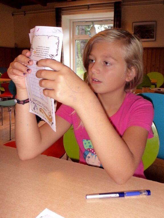a girl sitting at a table holding a piece of paper