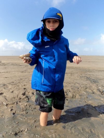 a boy standing in mud on a beach