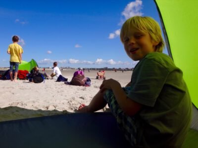 a boy sitting in a tent on a beach