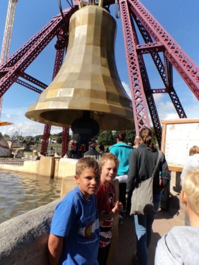 a group of kids standing in front of a large bell