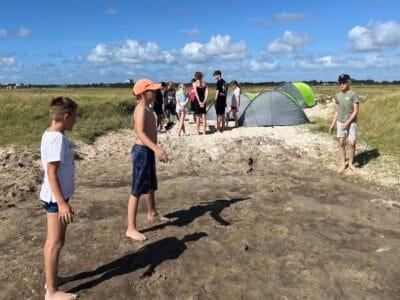 Kinder spielen am Strand, Zelt sichtbar.