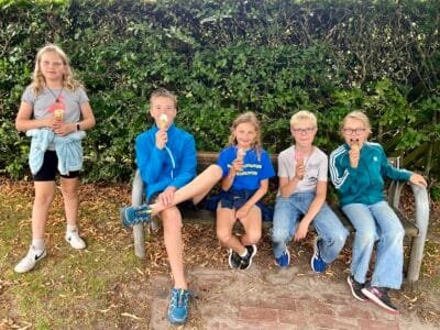 Fünf Kinder essen Eis auf Bank.